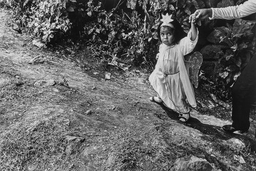 Black and white photo of a child in a dress with wings being held by an adult outdoors.