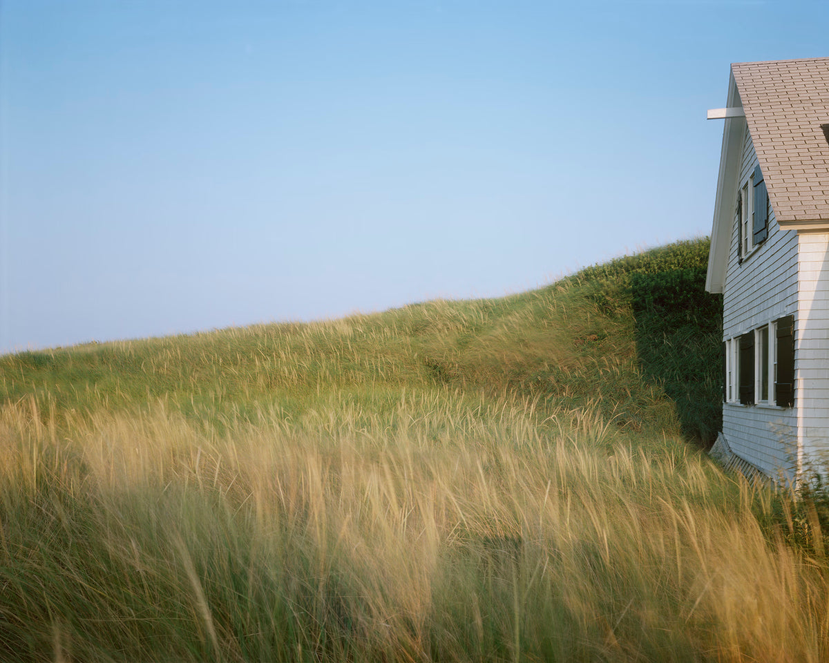 White house on a grassy hill with clear blue sky