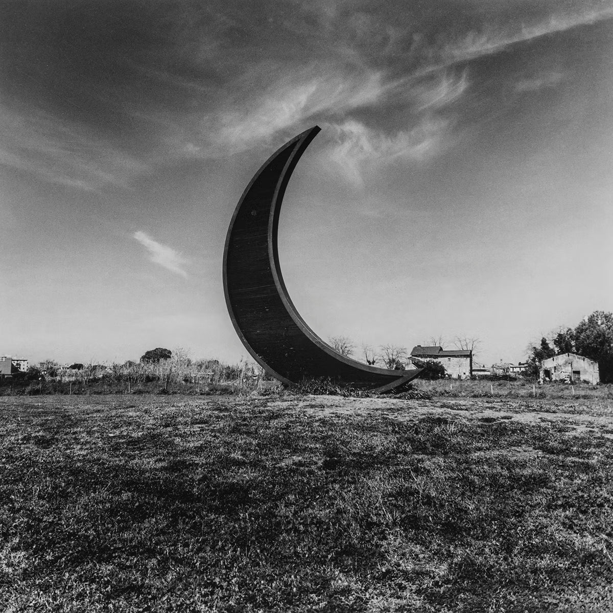 Large metal crescent sculpture in a field with a cloudy sky