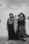 Two women standing side by side with a crocodile between them, against a textured wall.