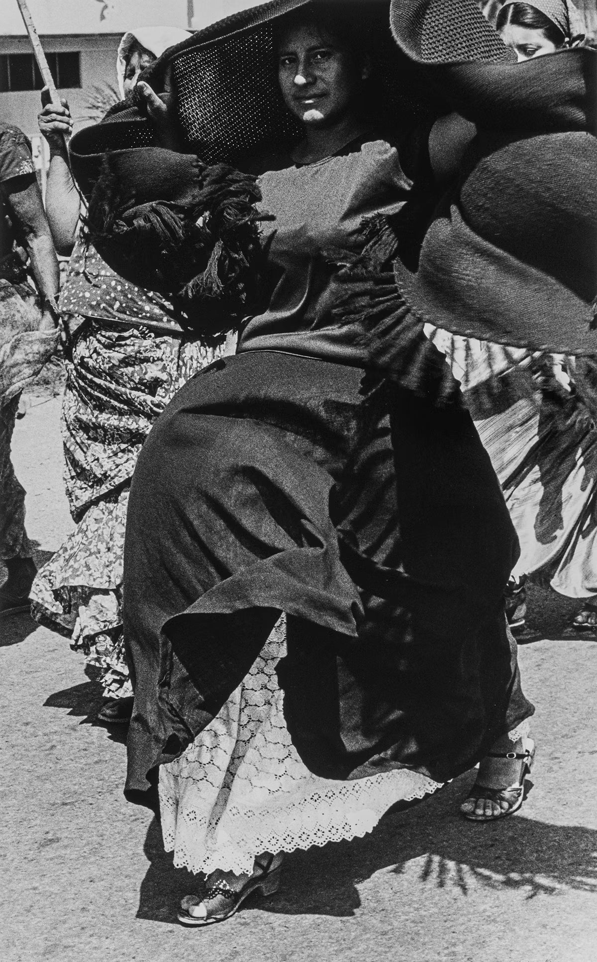 Woman in a traditional costume with a hat, surrounded by people in a street setting.