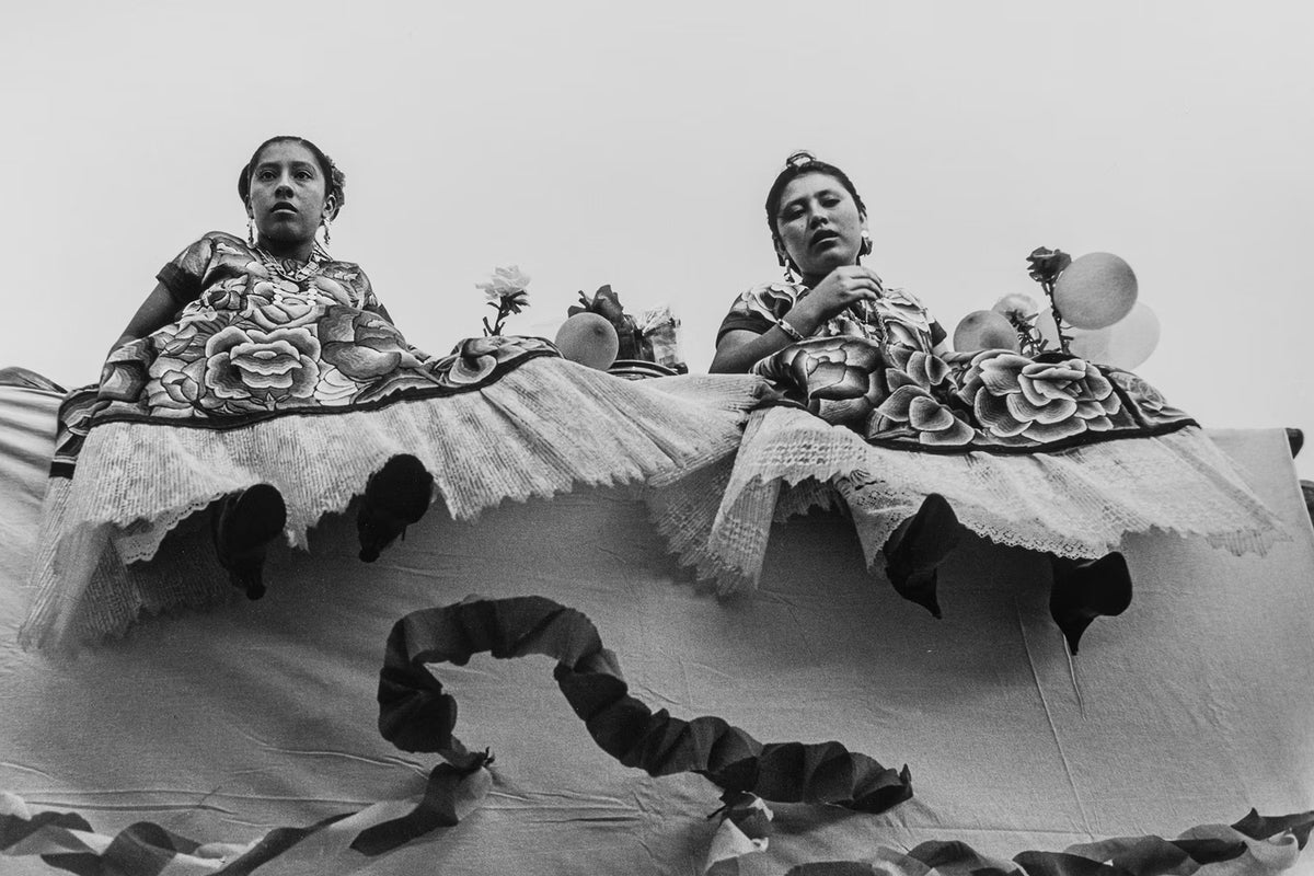 Two women in traditional attire sitting on a float with floral decorations.